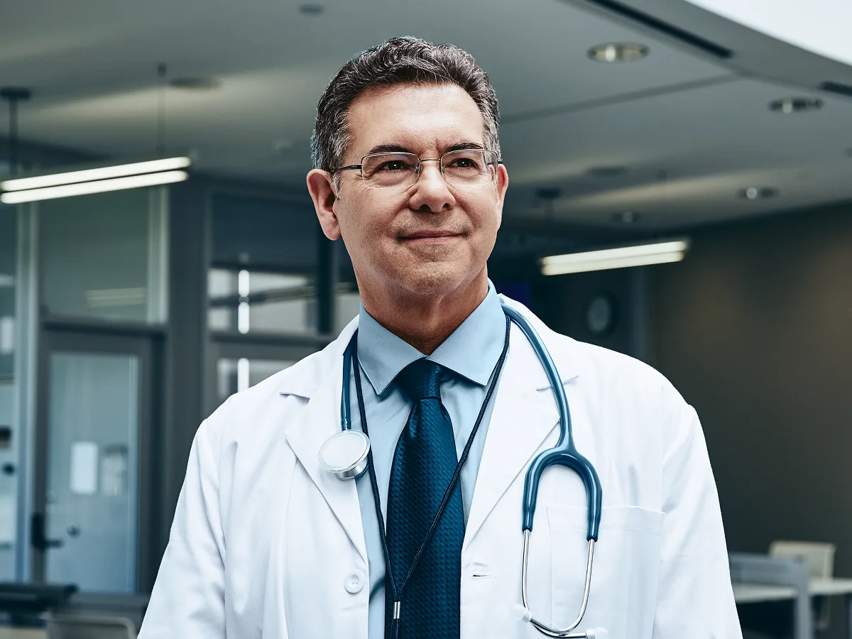 Médico usando jaleco branco, sorrindo com satisfação por contar com gestão financeira personalizada.